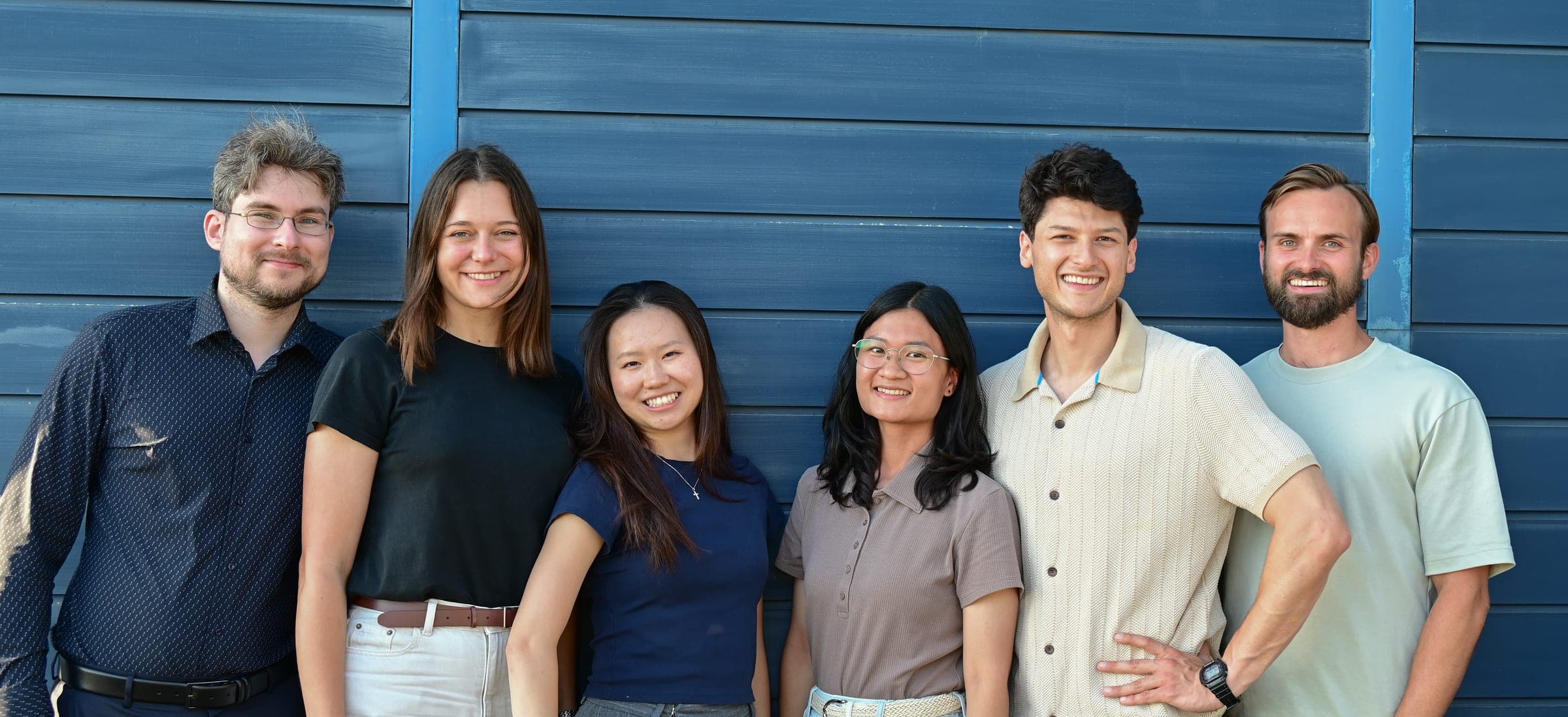 The AKIN team standing together in front of a blue wall